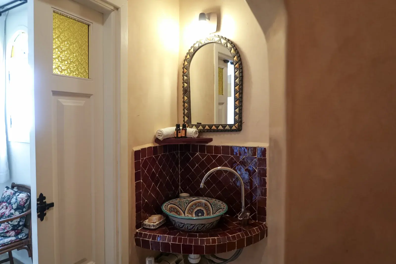 Bathroom sink and mirror in Double Twin Room 4 at Kasbah Rose guesthouse, featuring traditional Moroccan ceramic basin with ornate tile surround and decorative mirror frame, showcasing authentic craftsmanship in the bathroom design